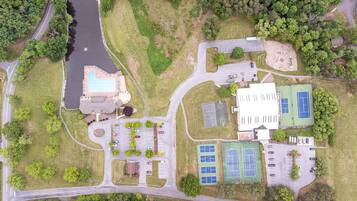An aerial view of a property with a swimming pool, tennis courts, and a parking lot.