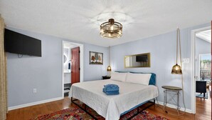 Een slaapkamer met een bed, een televisie, een kamerkleed met een patroon en een hanglamp.