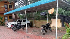 Ett överbyggt parkeringsområde med två motorcyklar, en vit bil och en byggnad med ett blått tak.