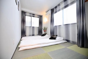 A room with two beds, a wall-mounted air conditioner, and a window with sheer curtains. - Spacious 4-bedroom apartment in heart of Osaka with AC (Osaka)