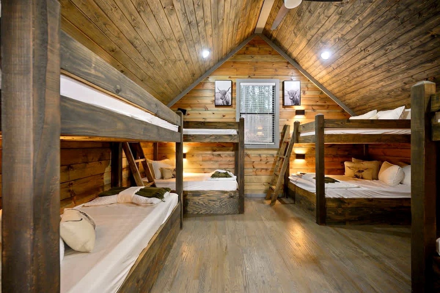 A cabin with bunk beds, wooden walls, a sloped ceiling, and a window with blinds.