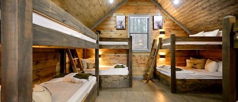 A cabin with bunk beds, wooden walls, a sloped ceiling, and a window with blinds.
