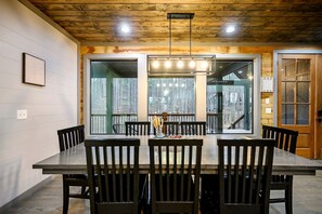 A dining area with a wooden table and chairs, large windows, and a view of the outdoors. - Luxury Forest Cabin with Hot Tub, Fire Pit & Game Room Near Broken Bow Lake, Broken Bow, Oklahoma (Broken Bow)