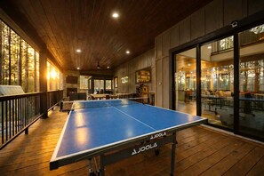 A ping pong table in a wooden-floored room with a glass door leading to an outdoor seating area. - Luxury Forest Cabin with Hot Tub, Fire Pit & Game Room Near Broken Bow Lake, Broken Bow, Oklahoma (Broken Bow)