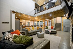 A spacious living area with a high ceiling, built-in wooden beams, and a staircase leading to an upper level. - Luxury Forest Cabin with Hot Tub, Fire Pit & Game Room Near Broken Bow Lake, Broken Bow, Oklahoma (Broken Bow)