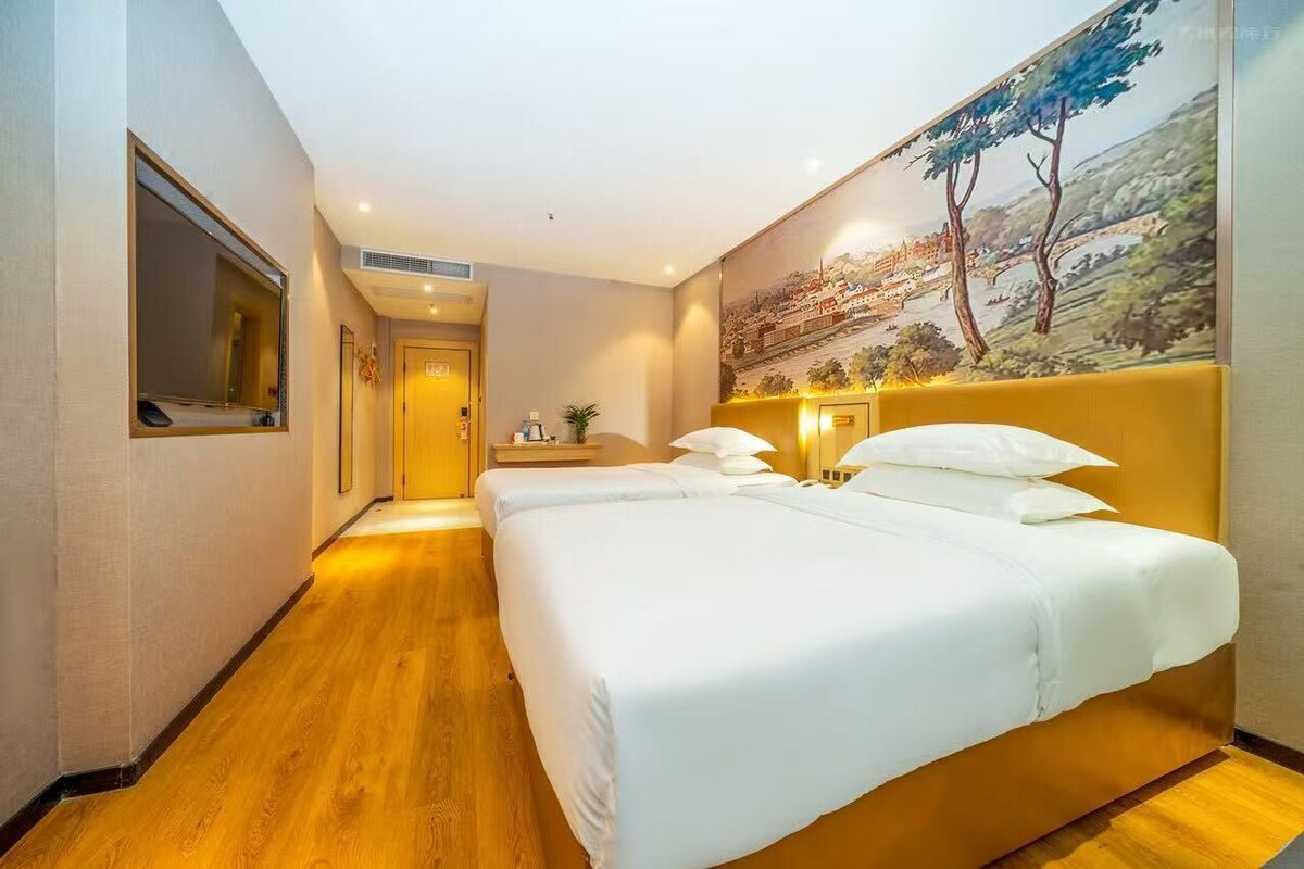 A hotel room with a large bed, a painting on the wall, and a wooden floor.