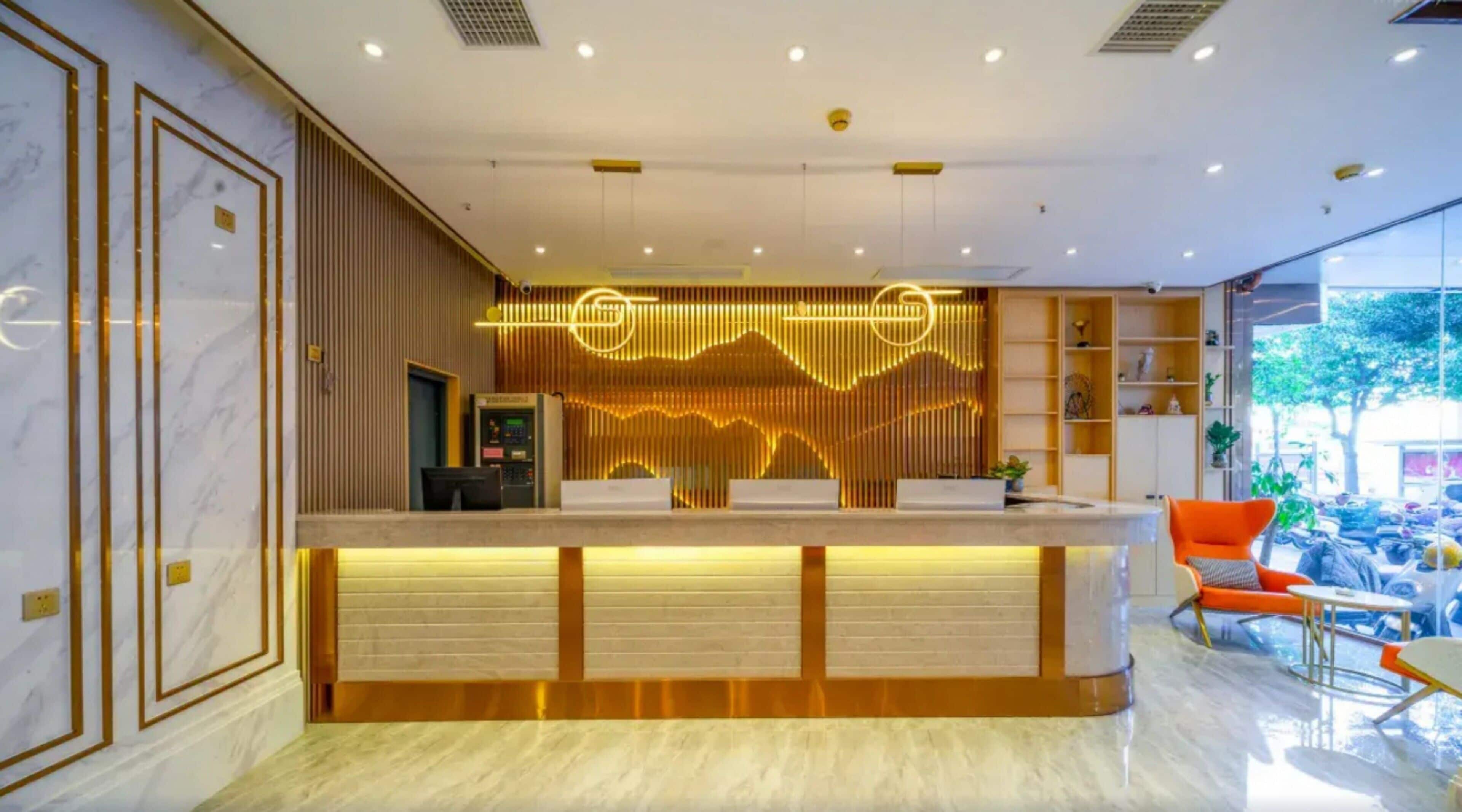Un comptoir d’accueil au design moderne, un espace détente avec des fauteuils orange et une vue sur l’extérieur grâce à de grandes fenêtres.