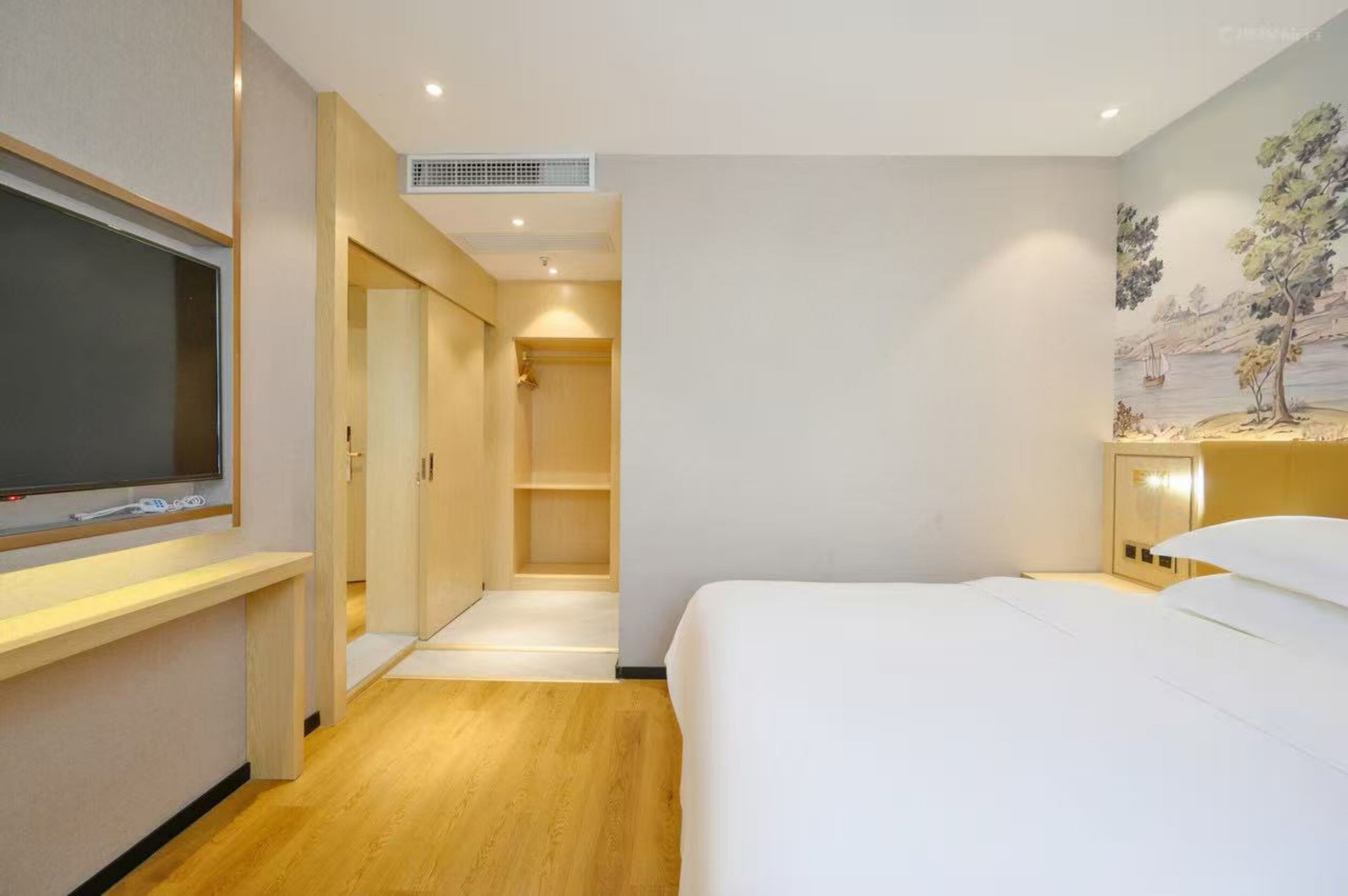 A hotel room with a bed, a TV, a wardrobe, and a painting on the wall.
