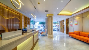 Een moderne hotel lobby met een receptiebalie, een zithoek en uitzicht op de straat.
