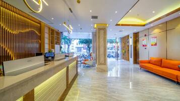 A modern hotel lobby with a reception desk, seating area, and a view of the street.
