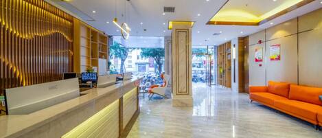 A modern hotel lobby with a reception desk, seating area, and a view of the street.