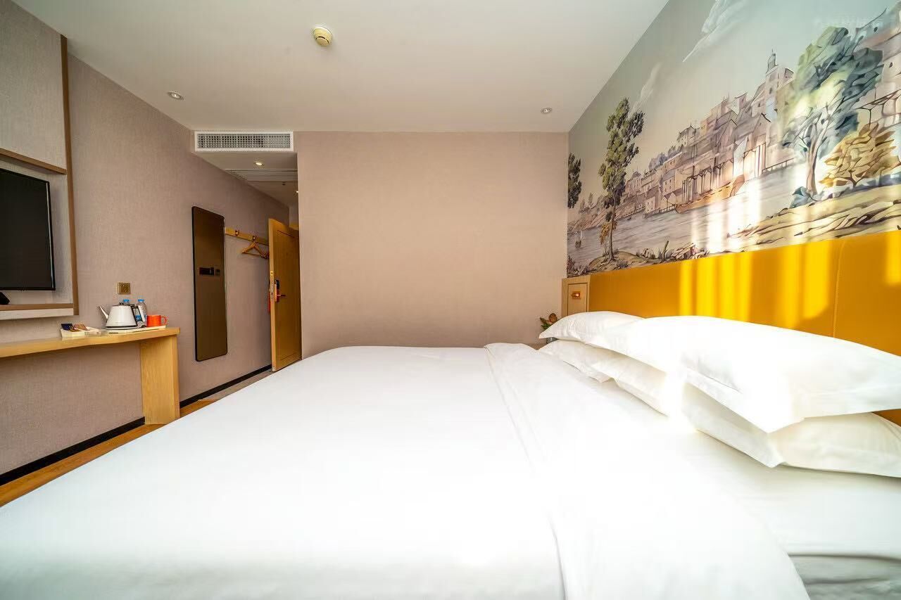 A hotel room with a bed, a TV, a desk, and a painting on the wall.