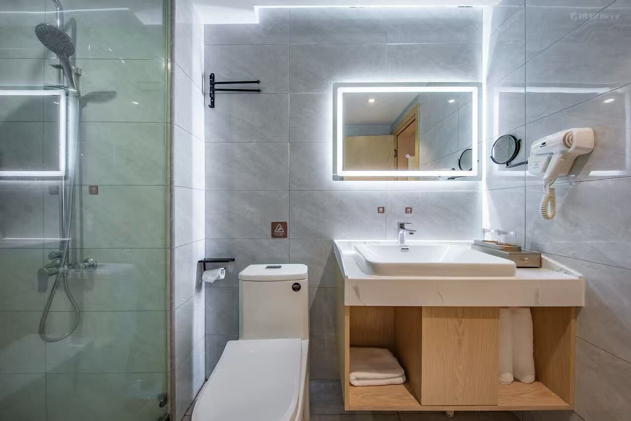 Ein modernes Badezimmer mit einer in Glas abgeschirmten Dusche, einem Waschtisch mit Spiegel und einem an der Wand befestigten Föhn.
