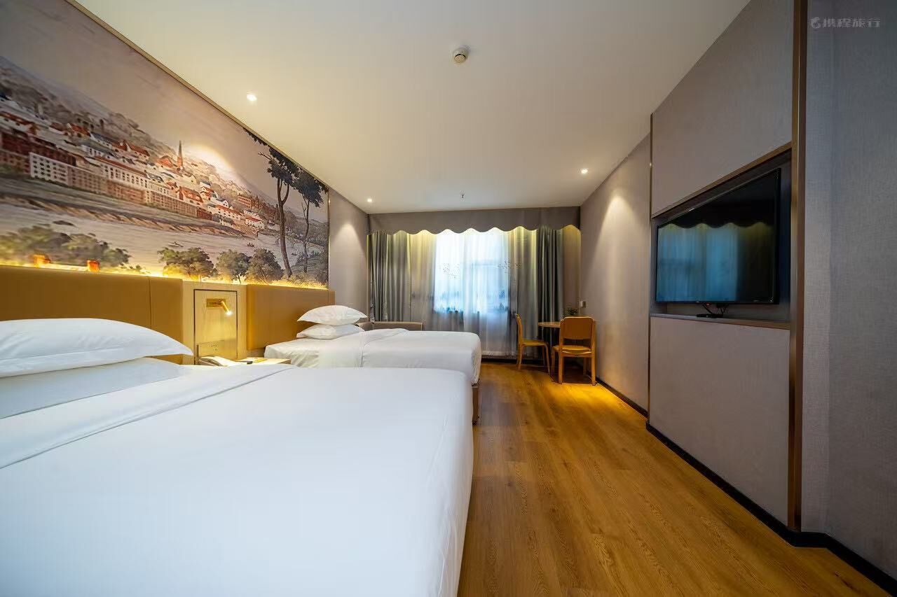 A hotel room with two beds, a TV, a desk, and a mural on the wall.