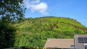 Uma encosta coberta por vegetação densa, um guarda-corpo de madeira e um edifício com painéis solares.