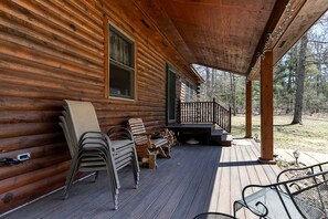 A log cabin with a porch, outdoor seating, and a view of the surrounding forest. - Cozy Forest Cabin with Fireplace Near Lake Michigan Beaches in Manistee, Michigan (Manistee)