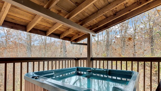 Een hottub onder een houten terras, met uitzicht op een bos.