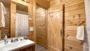 Een houten badkamer in een chalet, met een wastafel, spiegel en douchegordijn.
