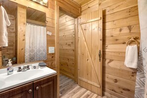 Baño de cabaña de madera con lavamanos, espejo y cortina de ducha.