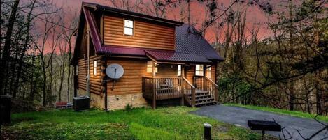 A log cabin with a porch, a satellite dish, and a driveway.