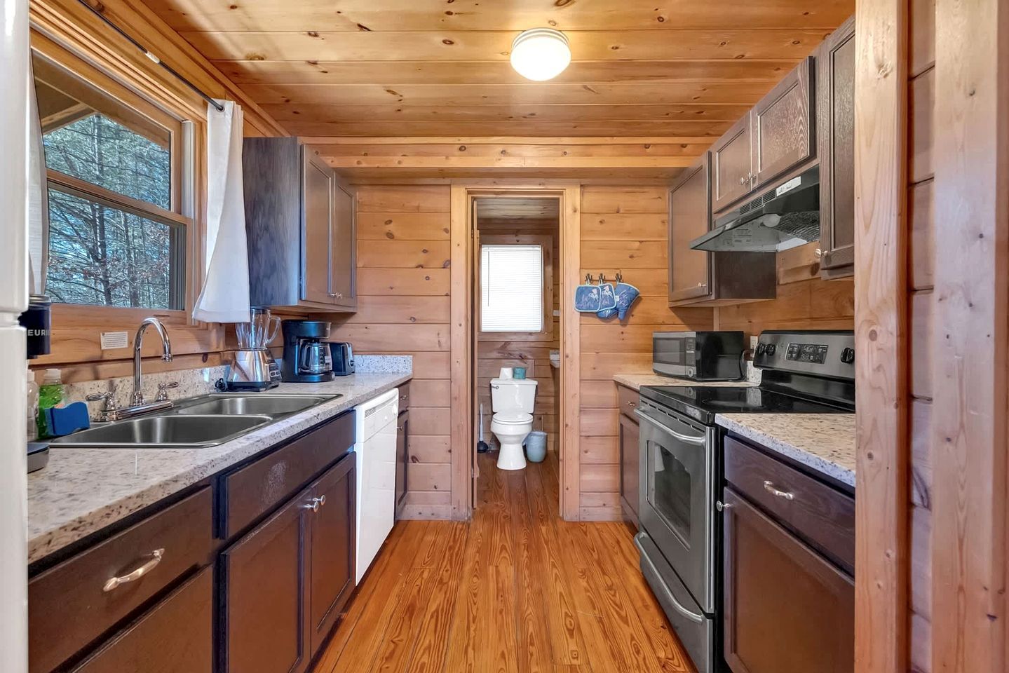 A wooden cabin-style kitchen with a sink, stove, microwave, and cabinets.