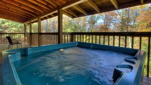 Een hottub onder een houten terras, met uitzicht op herfstbomen.