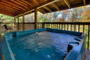 Un jacuzzi debajo de una terraza de madera con vistas a árboles otoñales.