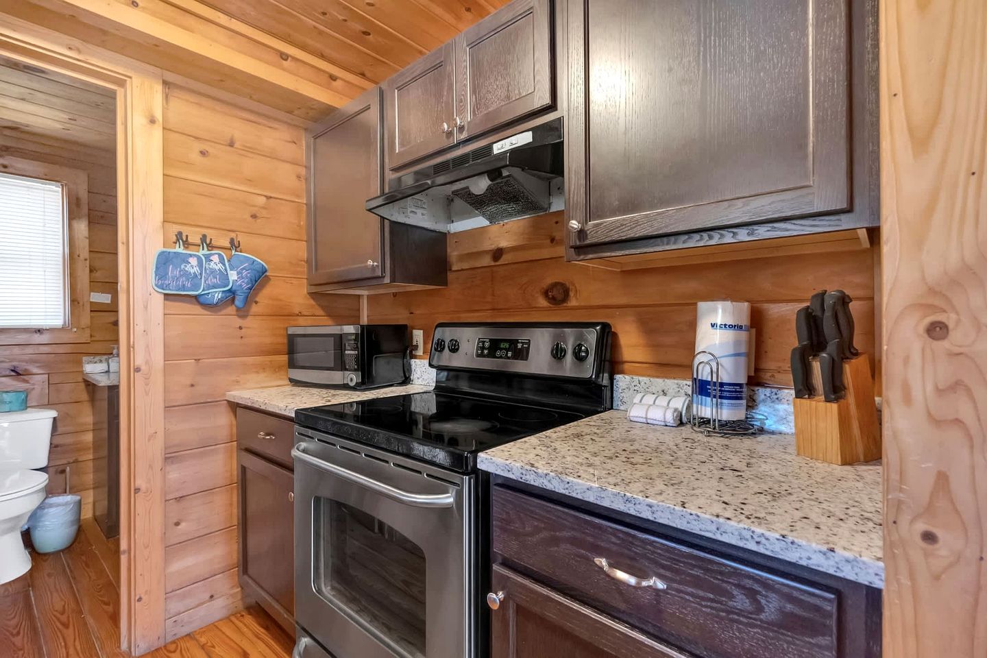 A compact kitchen with a microwave, stove, oven, and wooden cabinets.