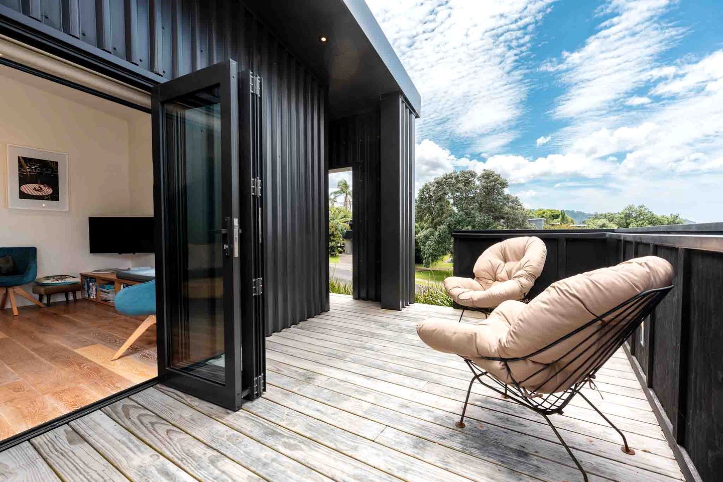 Et moderne opholdsrum med en træterrasse, en glasdør til udenom og et siddeområde med en stol.