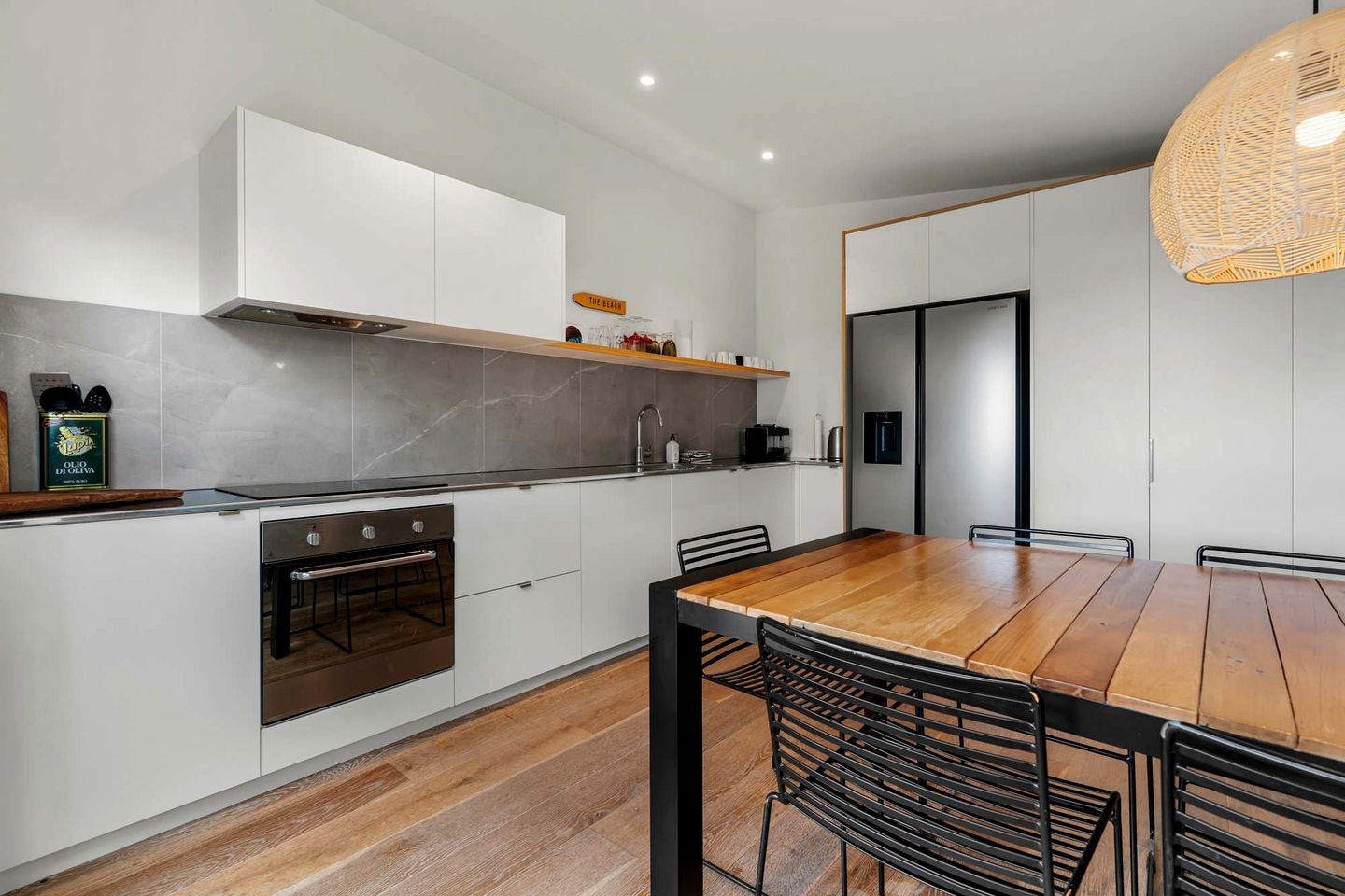 A modern kitchen with white cabinets, a wooden dining table, and black chairs.