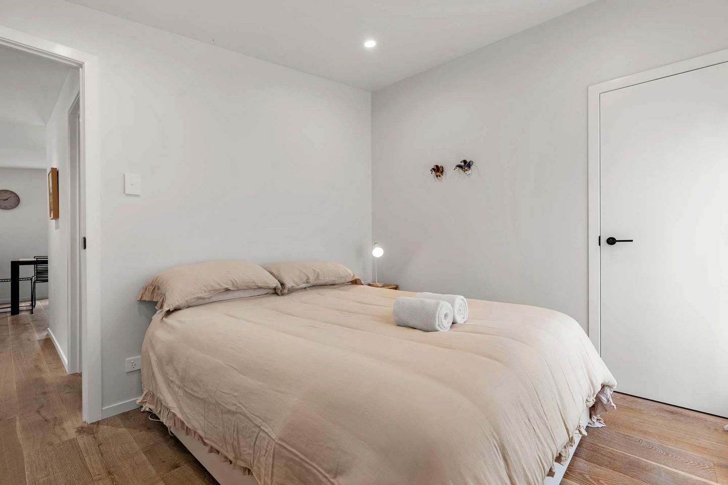 A bedroom with a bed, a nightstand, a wall clock, and a door.