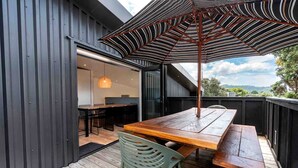 Un espacio de comedor al aire libre con una mesa y sillas de madera, un paraguas a rayas y vistas del paisaje.