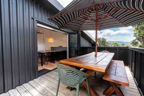 Een terras met een houten tafel en stoelen, een strepenpatroon paraplu en uitzicht op het landschap.