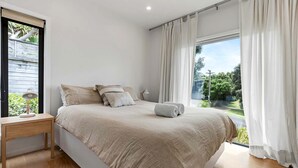 Un dormitorio con cama, mesita de noche, lámpara y vista a espacios verdes.