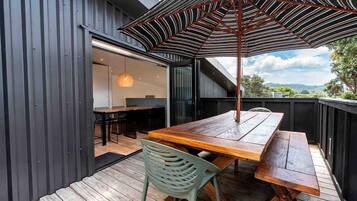 An outdoor dining area with a wooden table and chairs, a striped umbrella, and a view of the landscape.