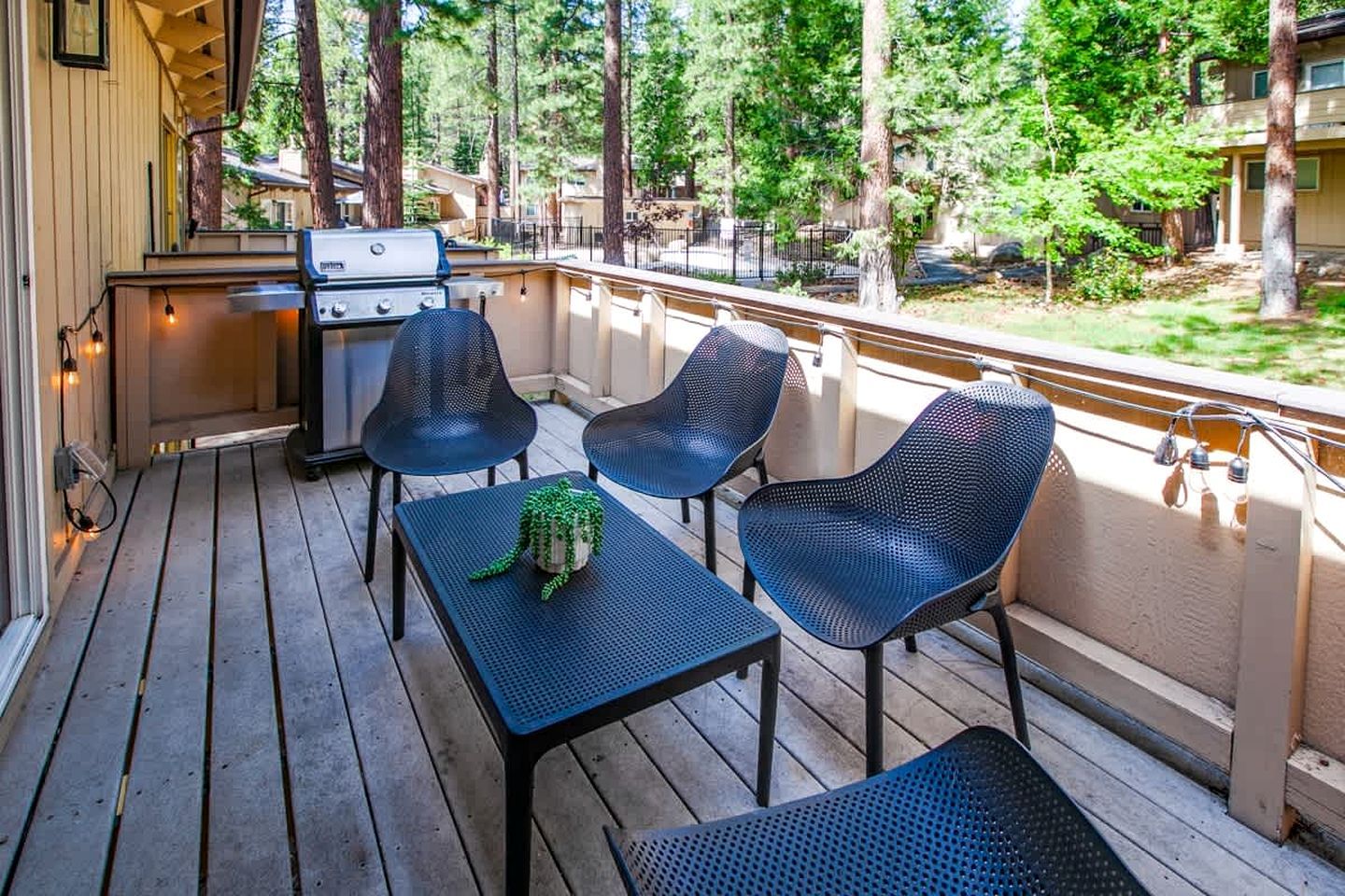 A covered deck with a grill, two chairs, and a table.