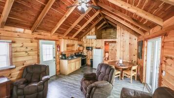 Interior de uma cabana de toras com sala de jantar, cozinha e dois poltronas de couro reclináveis.