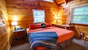 Quarto de cabana aconchegante com cama, duas mesas de cabeceira, uma janela com persianas e uma luminária em cada mesa.