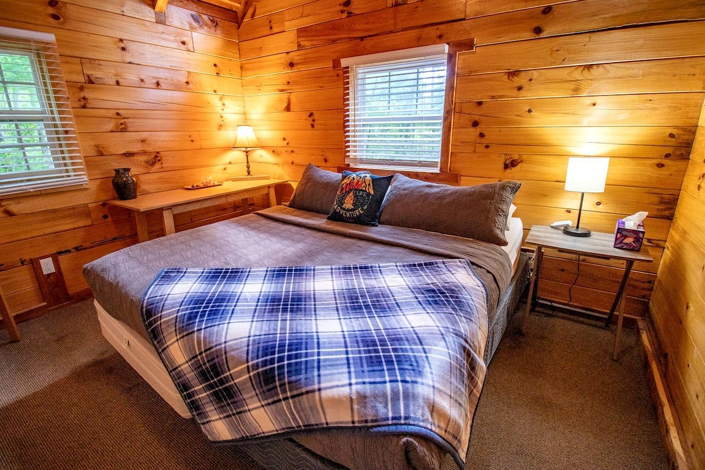 Une chambre à coucher dans un chalet en bois, avec un lit, deux tables de chevet, une lampe et une fenêtre avec des stores.