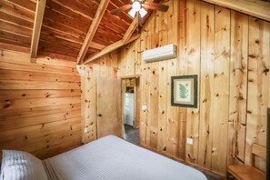 Een kamer met houten lambrisering, een bed, een plafondventilator en een airconditioning.