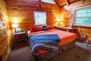 Una habitación de cabaña acogedora con una cama, dos mesitas de noche, un ventanal con persianas y una lámpara en cada mesita.