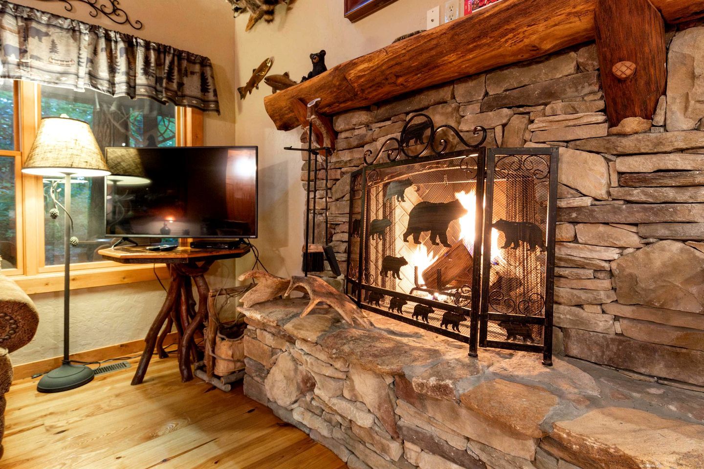 A stone fireplace with a TV on a wooden stand, a lamp, and a bear-themed screen.