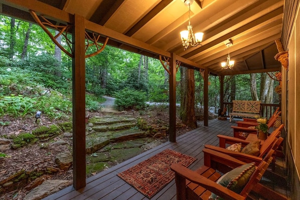 Une terrasse en bois couverte, dotée de bancs, et un sentier de pierres menant à une forêt.