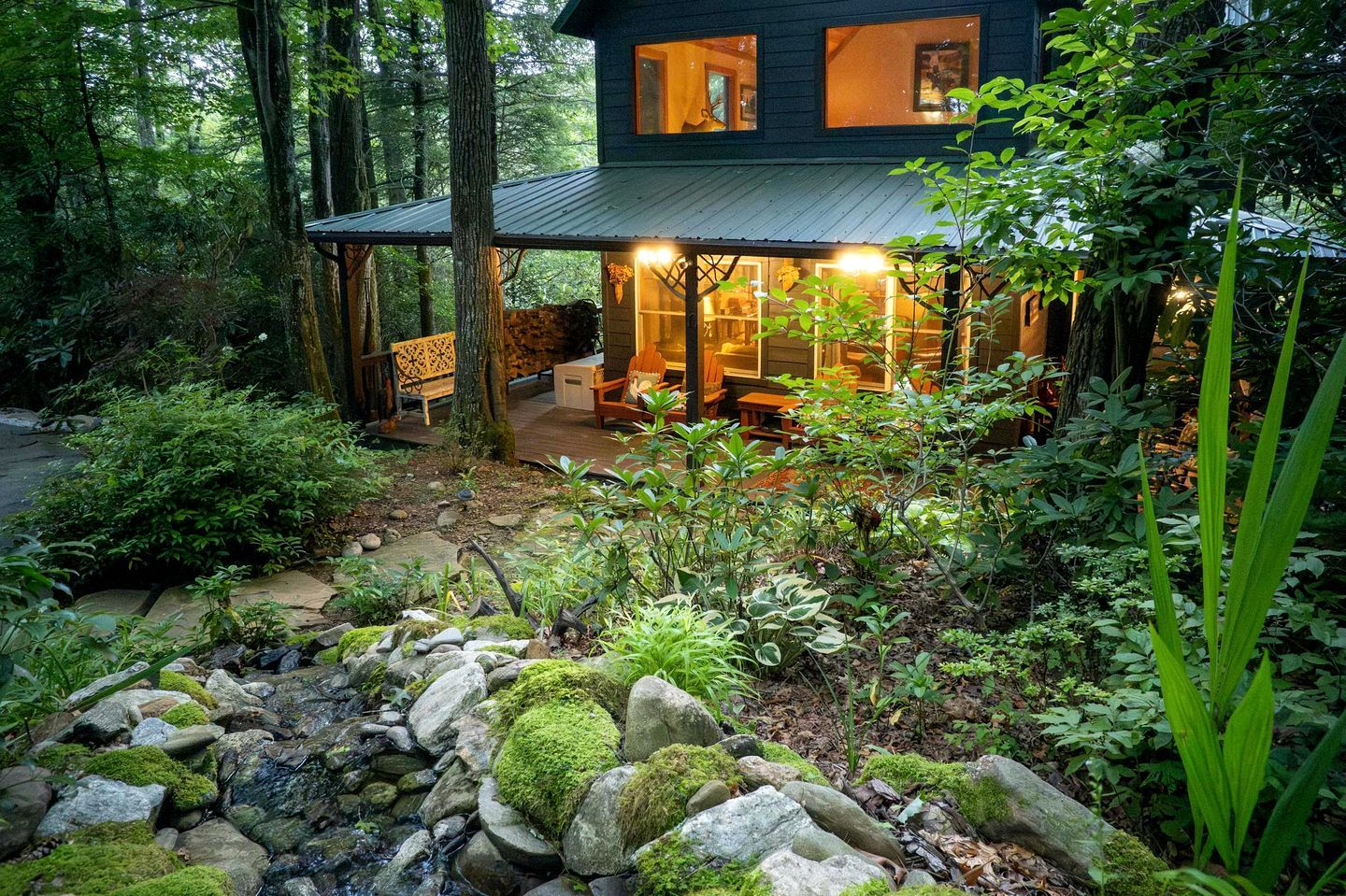 A rustic cabin with a covered porch, stone pathway, and lush greenery.