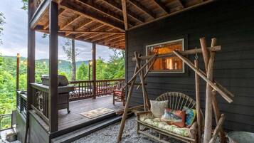 A wooden deck with a grill, a swing chair, and a view of the forest.