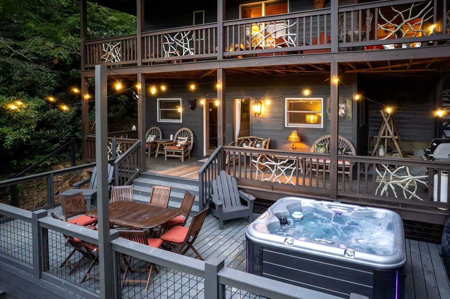 A two-story deck with outdoor seating, a hot tub, and string lights.