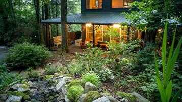 A rustic cabin with a covered porch, stone pathway, and lush greenery.