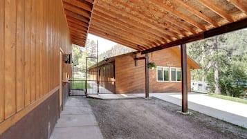 A covered outdoor area with a wooden floor, a metal gate, and a building with a sloped roof.