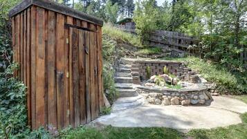 Ein Holler Schuppen, eine Feuerstelle aus Stein und ein Betonweg in einem Garten.