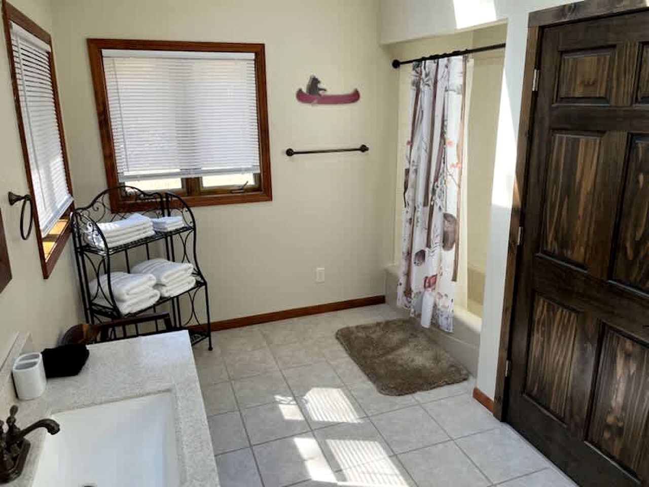Ein Badezimmer mit Waschbecken, Handtuchhalter, Fenster, Duschvorhang und Holztür.